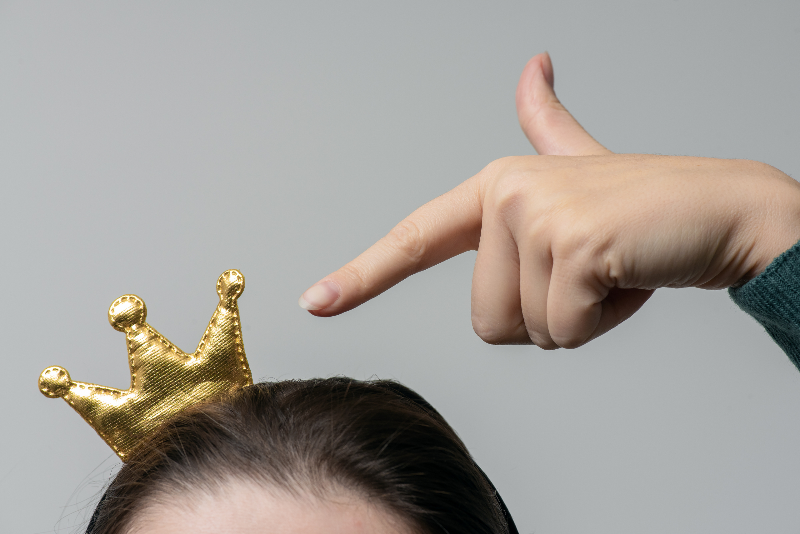 Frau zeigt mit ihrem Finger auf eine kleine Krone auf ihren Kopf